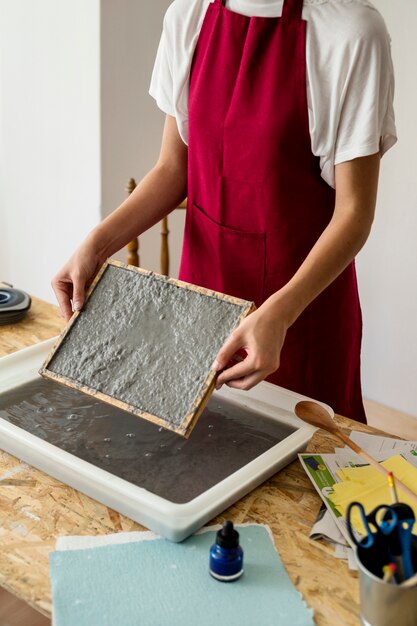 Woman's hand holding mold with pulp on wooden desk