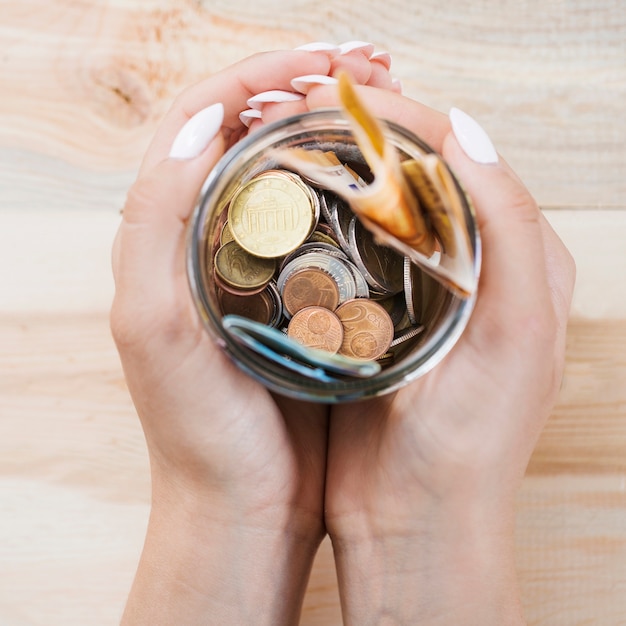 Free photo woman's hand holding saving in the jar against wooden background