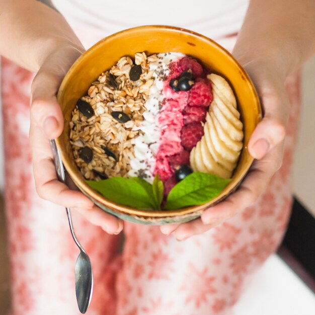 Woman's hand holding tasty oatmeal with berries and banana slices in bowl