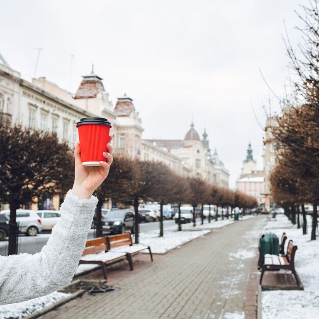 Рука женщины держит красную бумажную чашку перед аллеей в старом городе