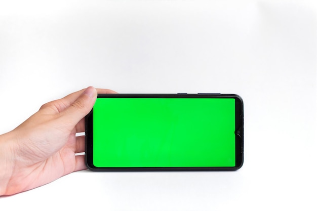 The woman's hand holds the smartphone in a horizontal position with a green screen on a white background. chroma key. mock up.