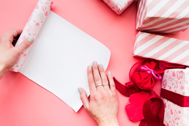 Woman's hand opening the rolled up gift paper with wrapped gift box on pink background