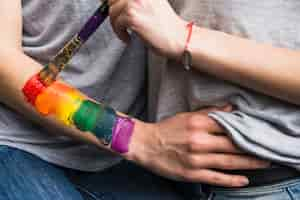 Free photo woman's hand painting the rainbow flag over the girlfriend's hand with paintbrush