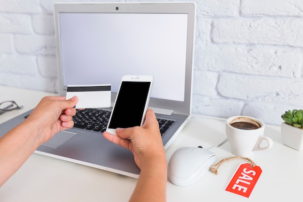 Woman's hand shopping online through mobile phone over the laptop