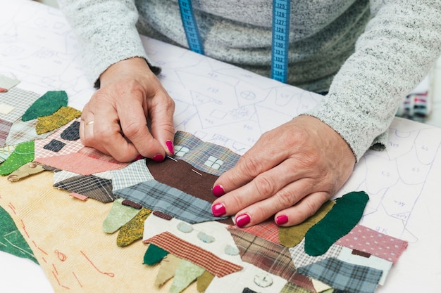 Woman's hand stitching fabric house with needle at workplace