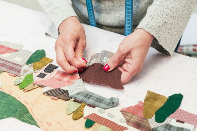 Woman's hand stitching fabric patch house with needle at workplace