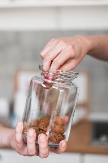 Woman's hand taking cookie from glass jar hold by a person