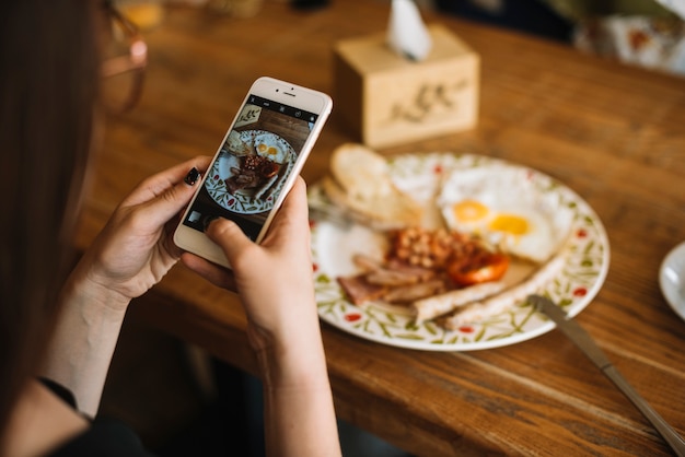 Рука женщины с фотографией завтрак на деревянный стол через сотовый телефон