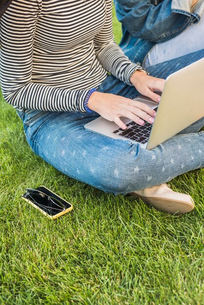 緑の草の上にサングラスと携帯電話の近くにラップトップを使用して女性の手