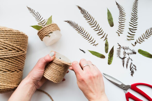 Woman's hand wrapping the string on candle with leaves and scissor on white background