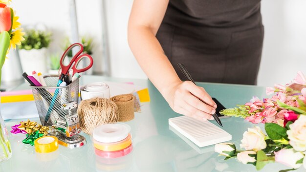 Woman's hand writing notes on notepad over glass desk