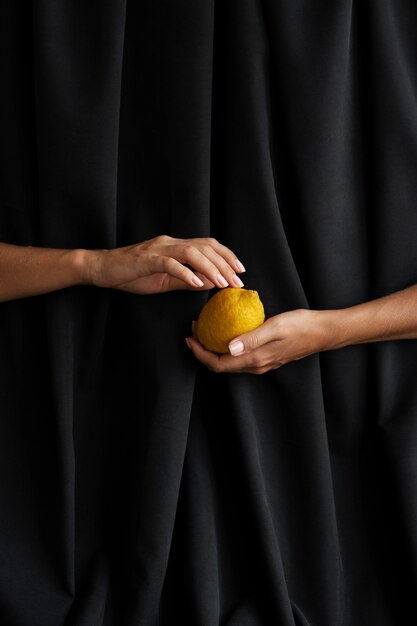 Woman's hands holding lemon with dark background