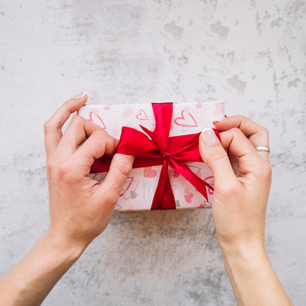 Free photo woman's hands near present box in wrap with red ribbon