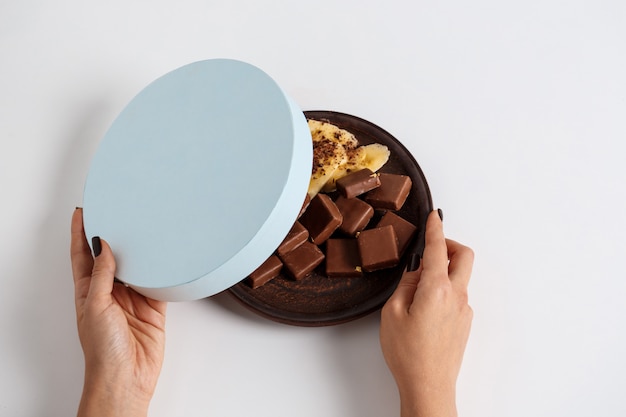 woman's hands opening box with chocolate and banana on white