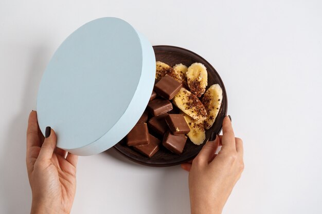 женские руки открывают коробку с шоколадом и бананом на белом