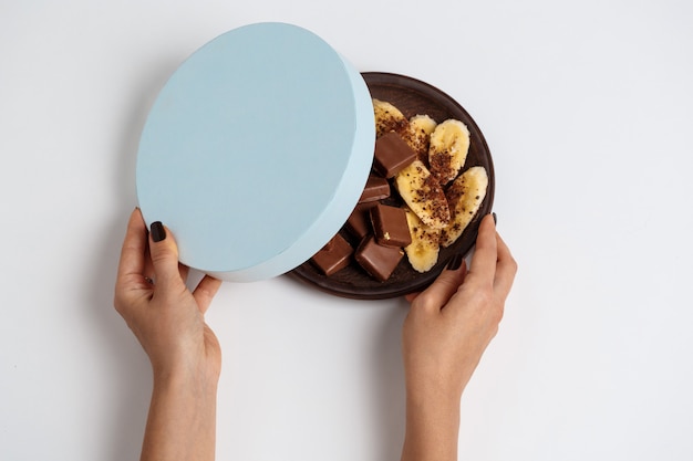 Foto gratuita mani di donna scatola di apertura con cioccolato e banana su bianco