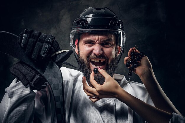 Женские руки с аккуратным маникюром кормят брутального эмоционального хоккеиста черным виноградом.