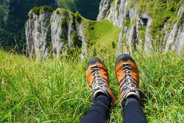 ロッキー山脈の景色を望む芝生の地面に対する女性のオレンジ色のハイキングシューズ