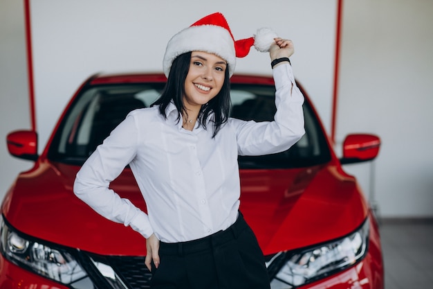 Woman in santa hat by the red car in a car showroom
