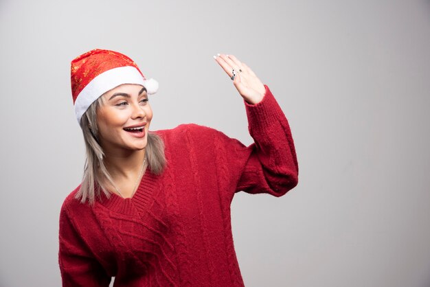 Woman in Santa hat greeting someone on gray background.