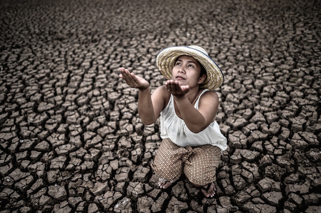 女性は空を見ながら座って、乾燥した天候の中で雨を求め、地球温暖化