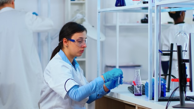 Woman scientist filling liquid test tube with pipette in modern equipped laboratory. Multiethnic medical stuff examining vaccine evolution using high tech researching diagnosis against covid19 virus