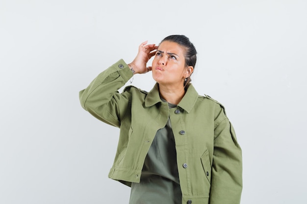 Woman scratching head in jacket, t-shirt and looking hesitant.