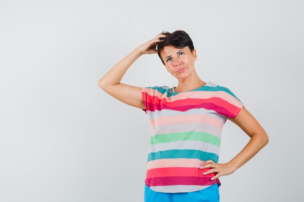 Woman scratching head in striped t-shirt, pants and looking pensive