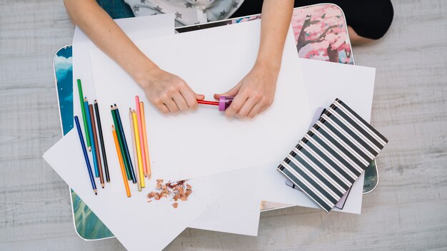 Woman sharpening pencil at table with papers and set of pencils