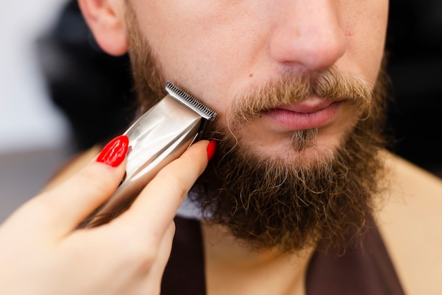Woman shaving her client's beard close-up
