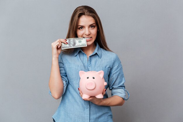 Женщина в рубашке держит копилку и деньги в руках