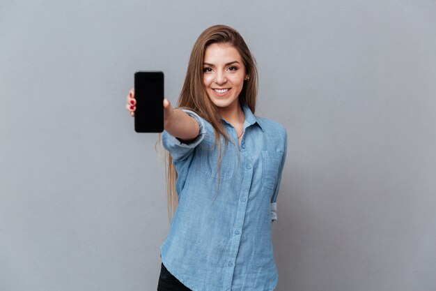 空白のスマートフォンの画面を示すシャツの女性