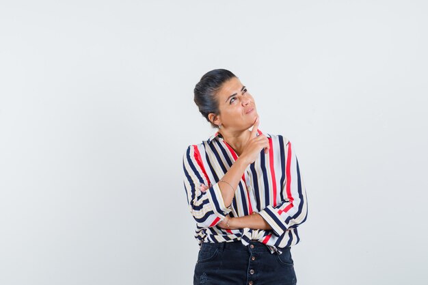 woman in shirt, skirt holding finger on chin and looking dreamy