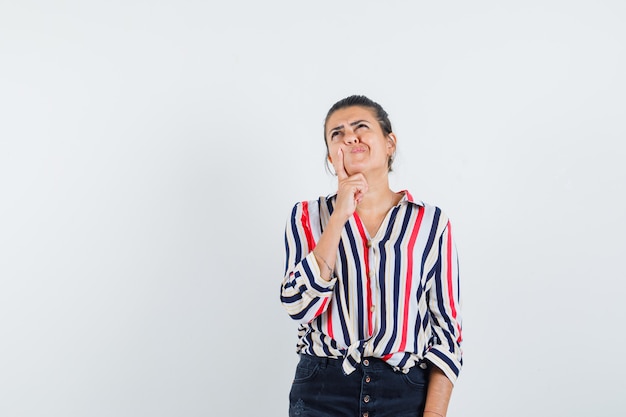 woman in shirt, skirt holding finger on chin and looking pensive