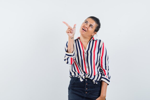 woman in shirt, skirt pointing at upper left corner and looking hopeful