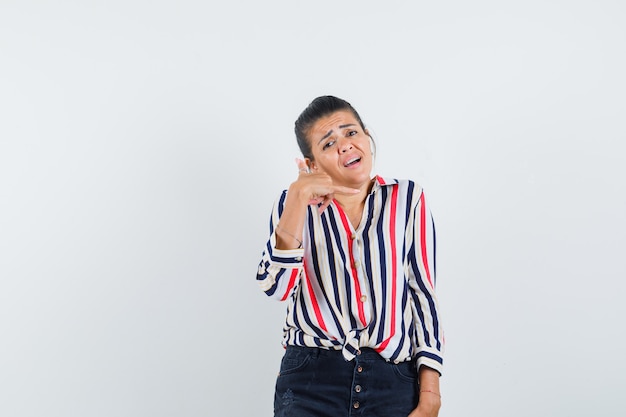 woman in shirt, skirt showing phone gesture and looking worried