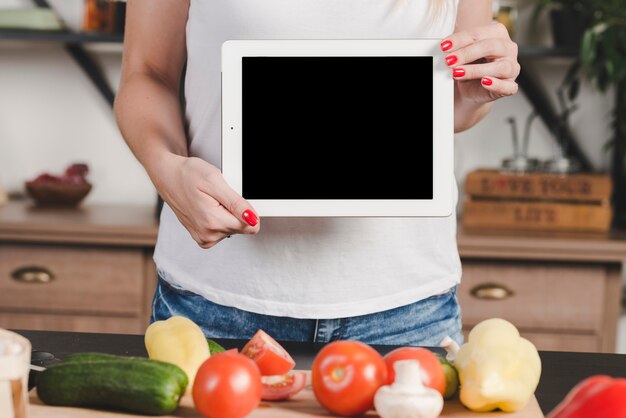 Woman showing blank digital tablet standing behind the vegetables on table