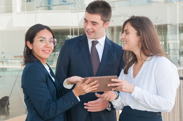 Woman showing colleagues data on tablet, looking at camera