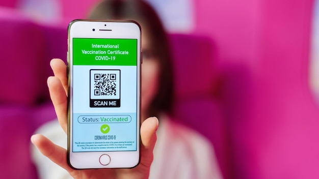 Woman showing COVID19 International Vaccination Certificate with QR code on a phone pink background