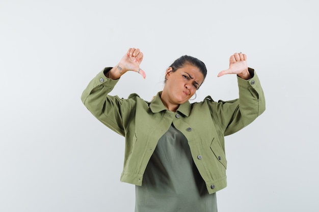 Woman showing double thumbs down in jacket, t-shirt and looking gloomy