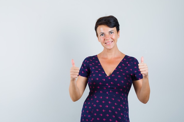 Woman showing double thumbs up in dress and looking cheerful.