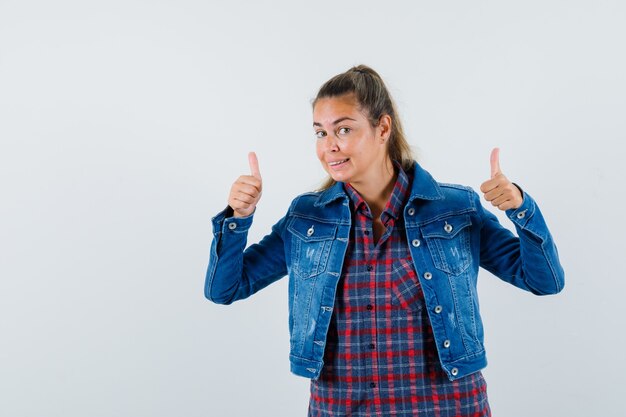 Woman showing double thumbs up in shirt, jacket and looking glad. front view.