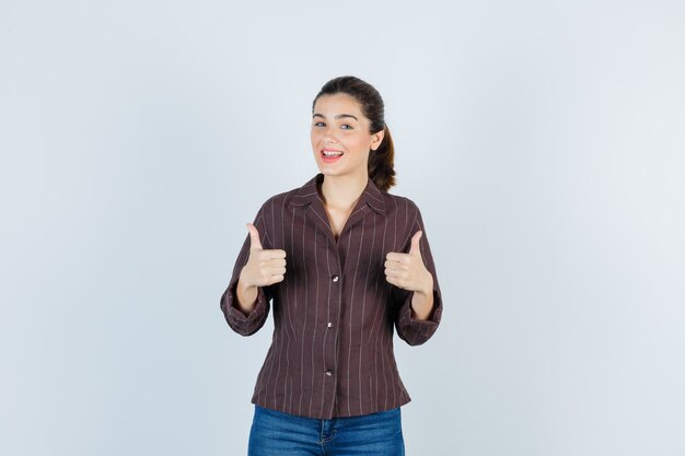 женщина показывает двойные пальцы вверх в рубашке, джинсах и выглядит счастливой. передний план.