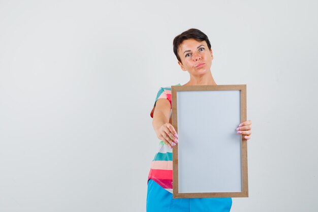 Woman showing empty frame in striped t-shirt, pants