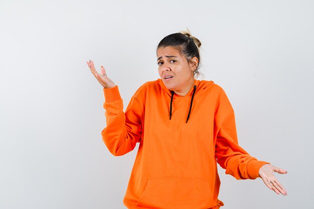 woman showing helpless gesture in orange hoodie and looking confused