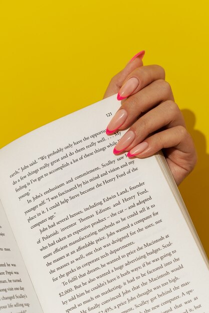 Foto gratuita donna che mostra la sua nail art sulle unghie con il libro