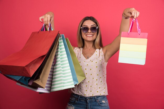 Woman showing her shopping bags on red wall . 