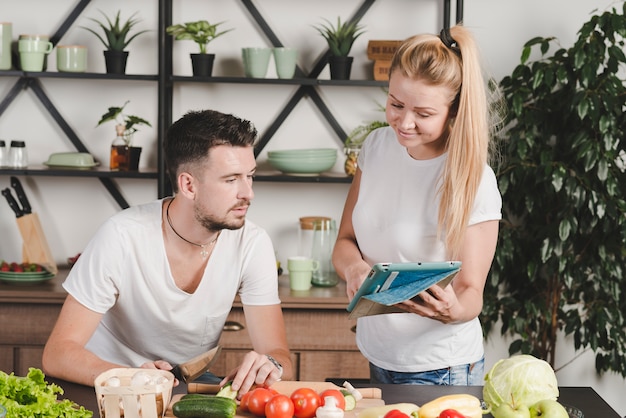 Woman showing laptop to man cutting vegetables