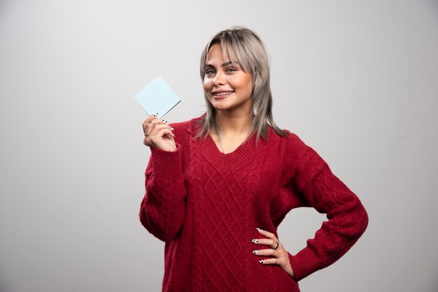 Woman showing memo pad and smiling on gray background.