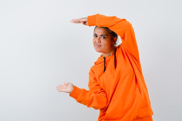 Free photo woman showing size sign in orange hoodie and looking confident